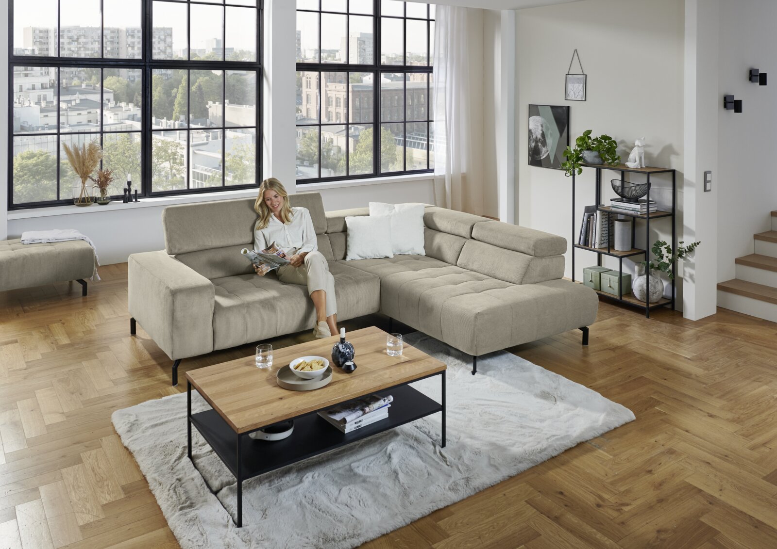 Beiges L-förmiges Ecksofa mit breiter Ottomane und schwarzen Metallfüßen in modernem Wohnzimmer, Frontansicht leicht schräg von links