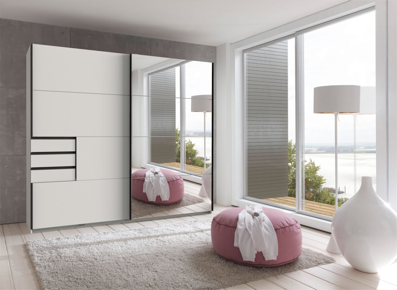 Moderner Schwebetürenschrank mit zwei Türen, teilweise verspiegelt, in einem hellen Raum mit Blick auf große Fenster. Perspektive von schräg vorne.