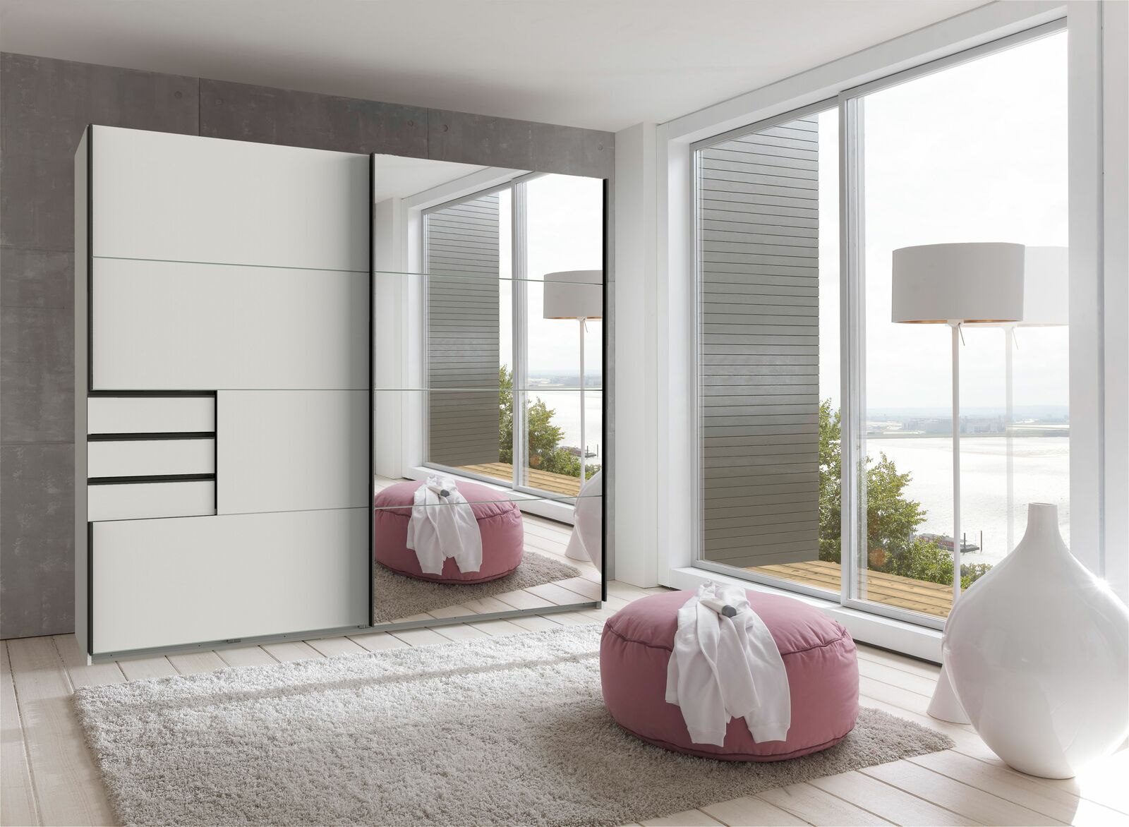 Moderner Schwebetürenschrank mit zwei Türen, teilweise verspiegelt, in einem hellen Raum mit Blick auf große Fenster. Perspektive von schräg vorne.