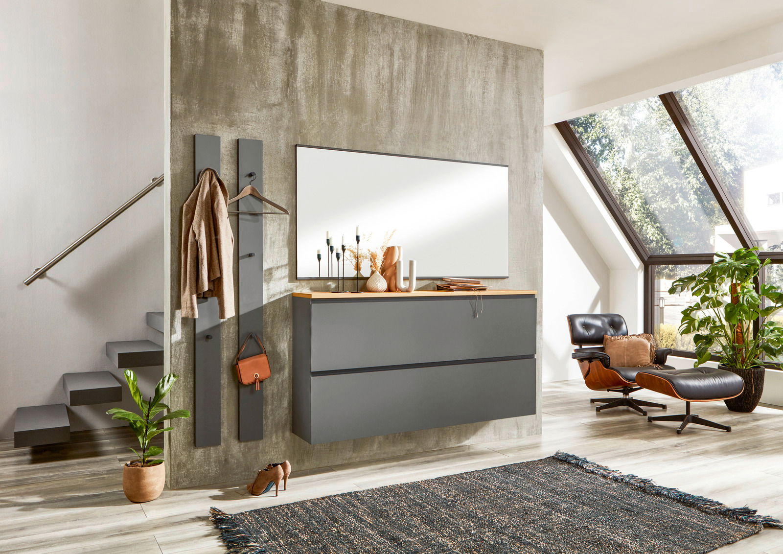 Moderne Garderobeneinrichtung mit Spiegel, Hängeschrank und Garderobenpaneel in einem stilvollen Raum mit Treppe und großem Fenster, seitliche Perspektive.