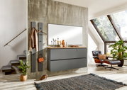 Moderne Garderobeneinrichtung mit Spiegel, Hängeschrank und Garderobenpaneel in einem stilvollen Raum mit Treppe und großem Fenster, seitliche Perspektive.