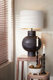 Moderner Lampenschirm Zylinder in Weiß auf dunklem, kugelförmigem Lampenfuß, seitliche Perspektive mit Kerzen und Dekoration.