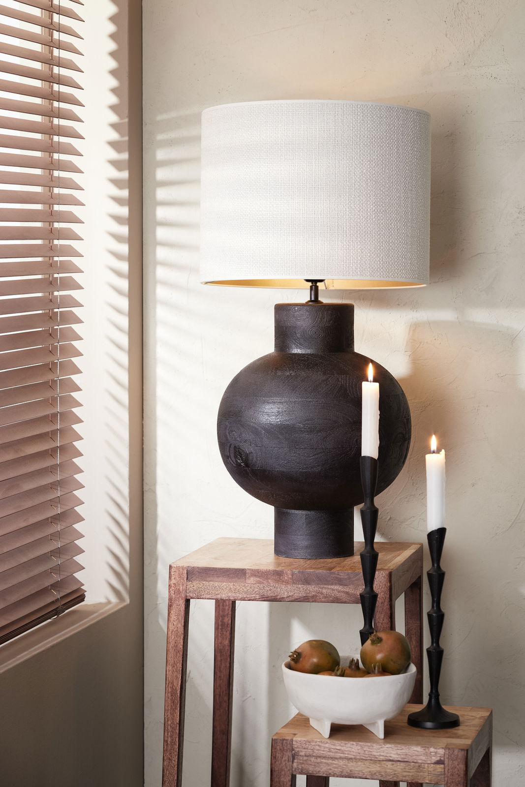 Moderner Lampenschirm Zylinder in Weiß auf dunklem, kugelförmigem Lampenfuß, seitliche Perspektive mit Kerzen und Dekoration.