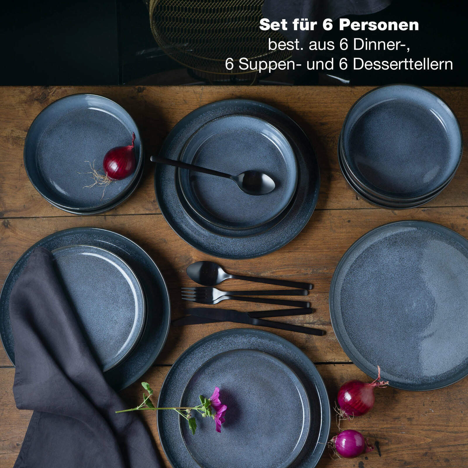 Vogelperspektive auf ein 18-teiliges blaues Tafelservice für 6 Personen, bestehend aus Dinner-, Suppen- und Desserttellern, auf einem Holztisch arrangiert mit Besteck, Zwiebeln und einer Blume.