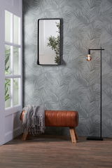 Bank aus braunem Leder mit Holzbeinen, seitliche Perspektive, dekoriert mit einer grauen Decke, vor einer Wand mit Pflanzenmuster.