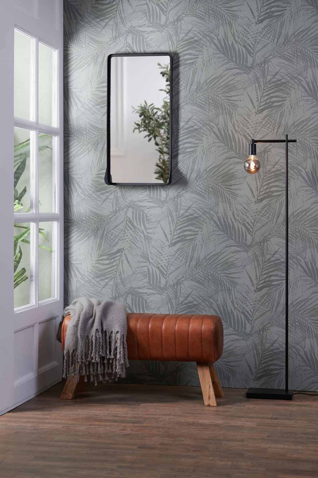 Bank aus braunem Leder mit Holzbeinen, seitliche Perspektive, dekoriert mit einer grauen Decke, vor einer Wand mit Pflanzenmuster.