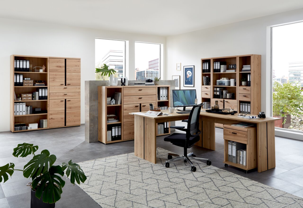 Moderne Büromöbel in einem hellen Raum mit großen Fenstern, bestehend aus Schreibtischen, Aktenschränken und Regalen aus Holz. Perspektive von vorne links.