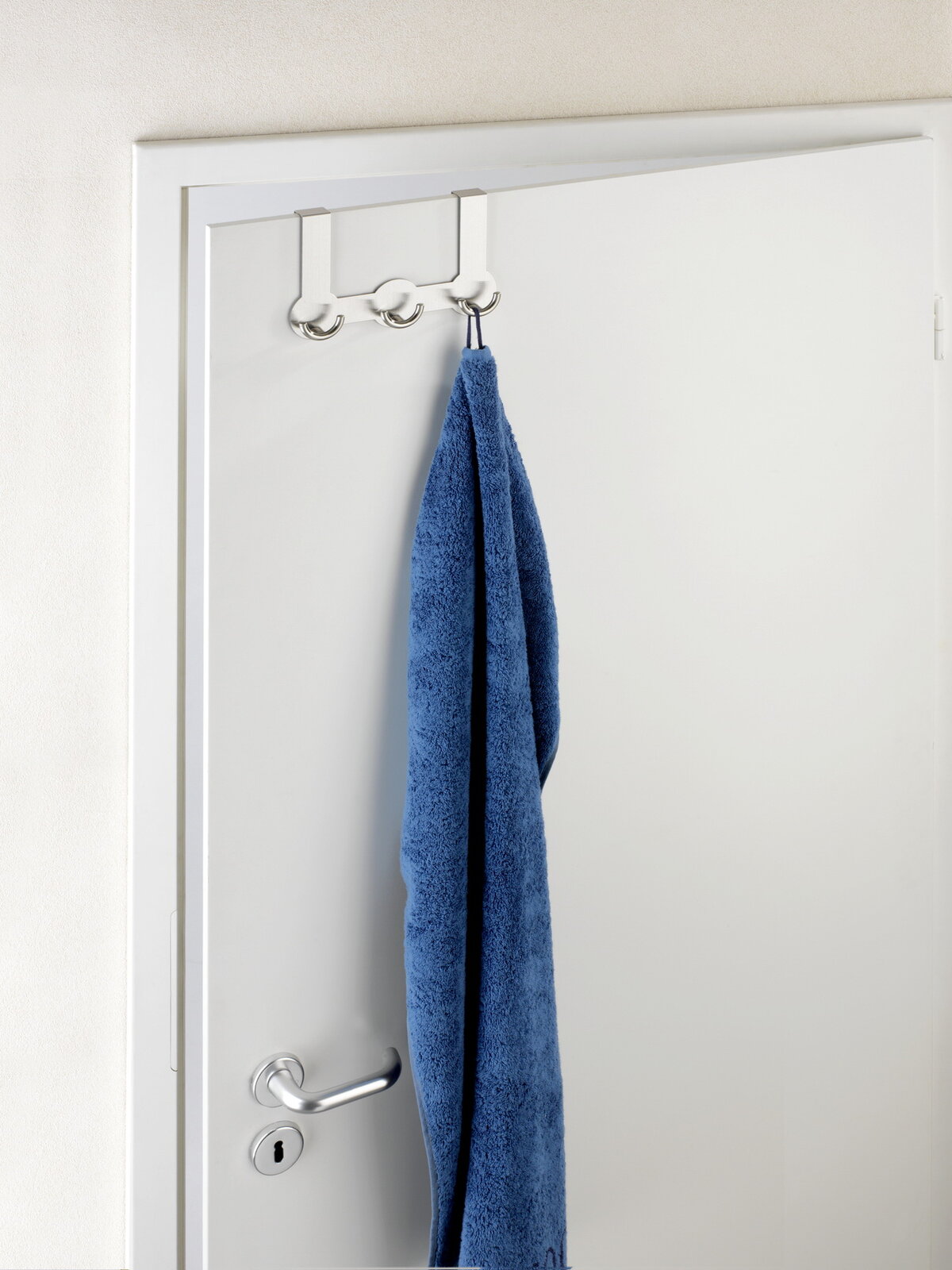Edelstahl Türgarderobe Rondo mit drei Haken, von vorne betrachtet, an einer weißen Tür mit einem blauen Handtuch.
