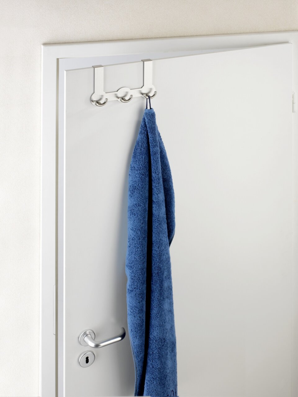 Edelstahl Türgarderobe Rondo mit drei Haken, von vorne betrachtet, an einer weißen Tür mit einem blauen Handtuch.