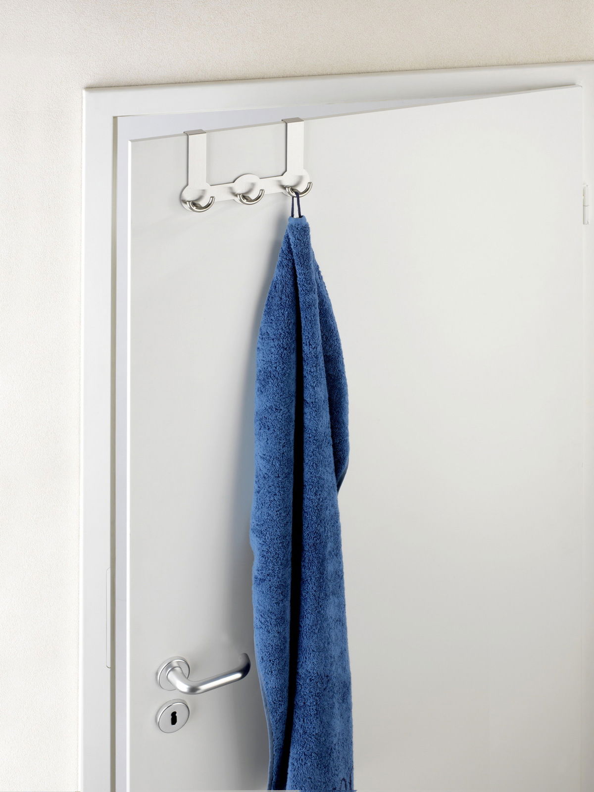 Edelstahl Türgarderobe Rondo mit drei Haken, von vorne betrachtet, an einer weißen Tür mit einem blauen Handtuch.