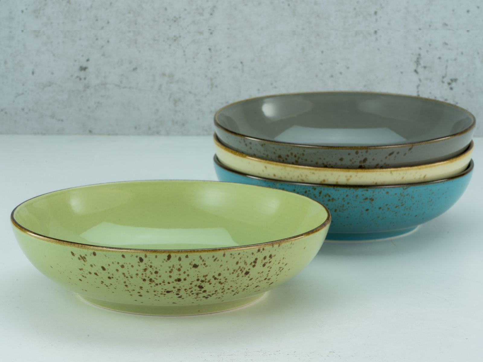 Vier Poke Bowls in verschiedenen Farben, gestapelt auf einer weißen Oberfläche, aus seitlicher Perspektive fotografiert.