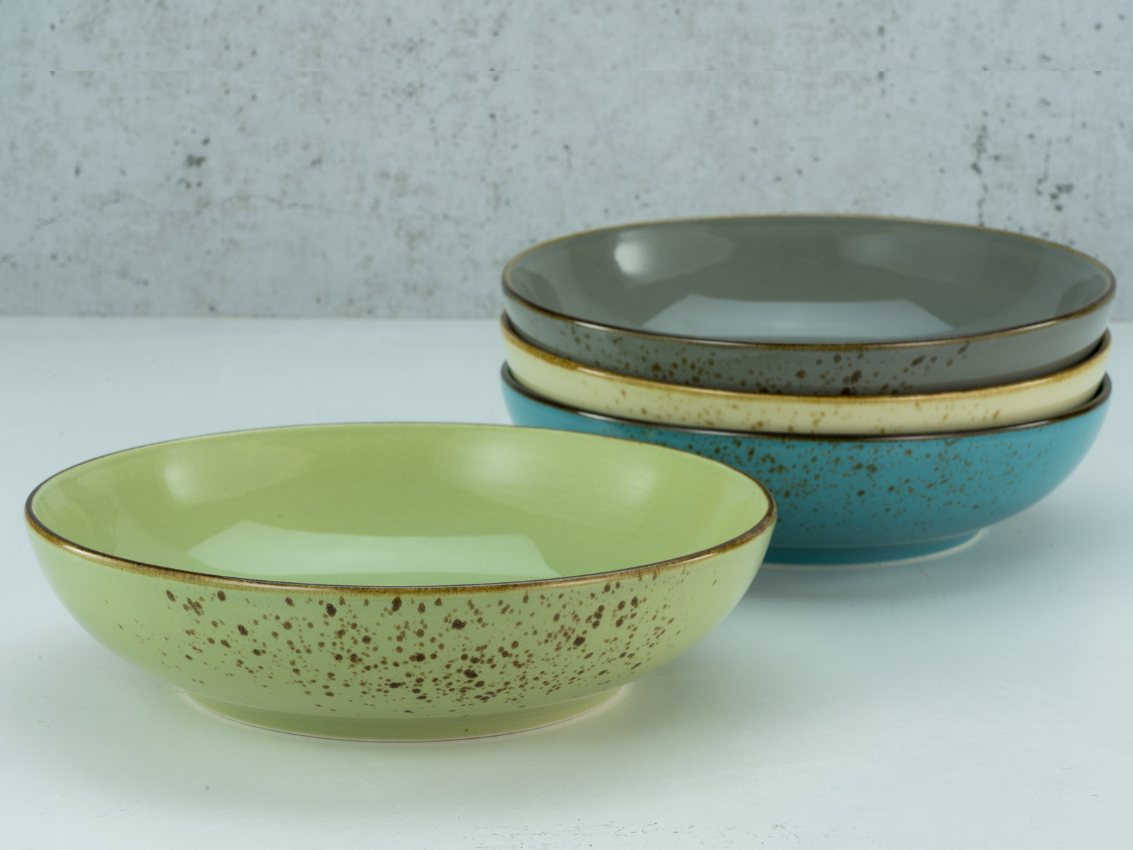 Vier Poke Bowls in verschiedenen Farben, gestapelt auf einer weißen Oberfläche, aus seitlicher Perspektive fotografiert.