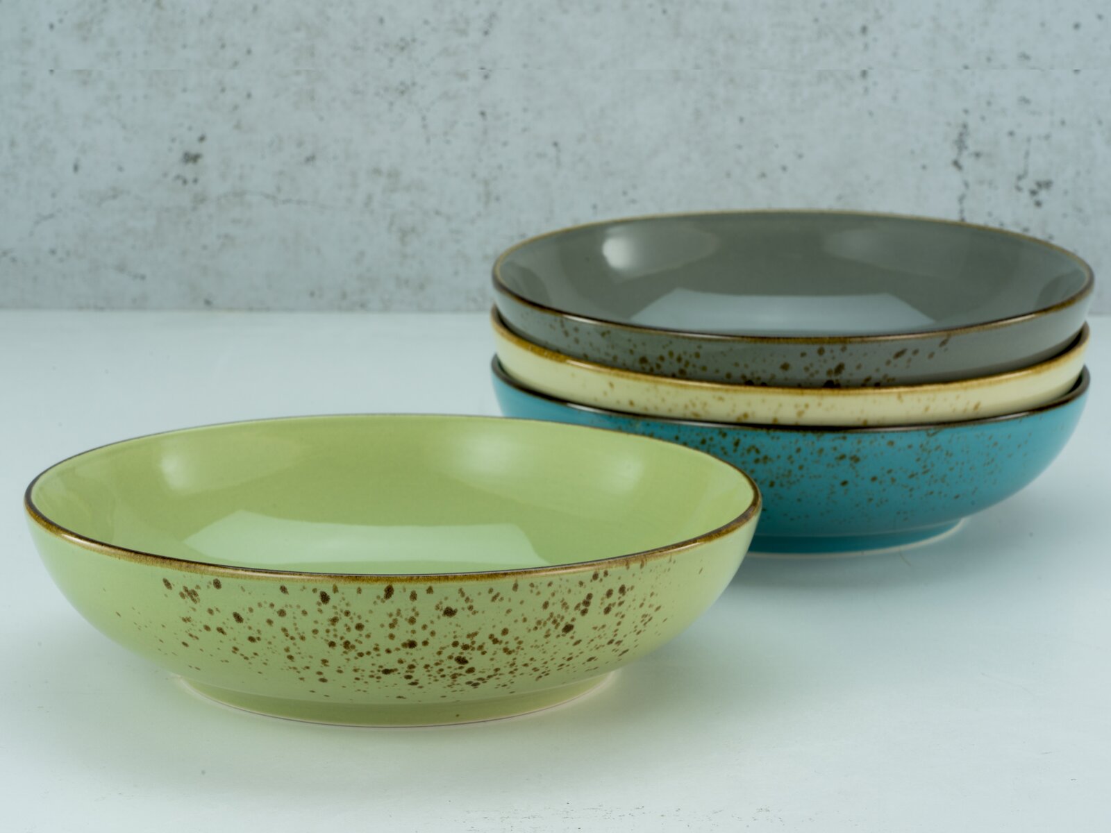 Vier Poke Bowls in verschiedenen Farben, gestapelt auf einer weißen Oberfläche, aus seitlicher Perspektive fotografiert.