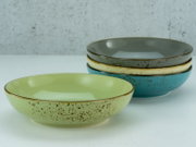 Vier Poke Bowls in verschiedenen Farben, gestapelt auf einer weißen Oberfläche, aus seitlicher Perspektive fotografiert.