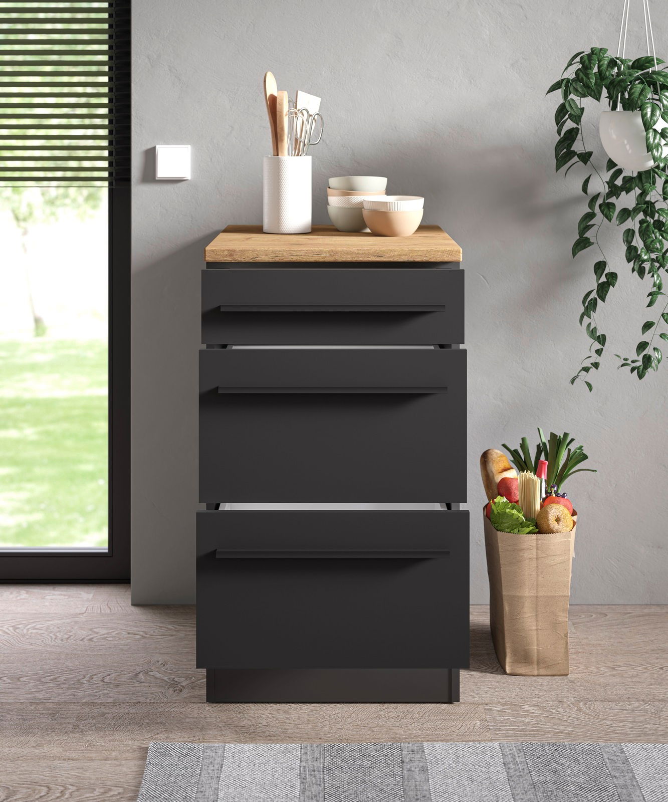 Moderner Unterschrank 50A in dunklem Design mit Holzplatte, frontal fotografiert, dekoriert mit Küchenutensilien und Schalen, neben einer Pflanze und einer Einkaufstüte.