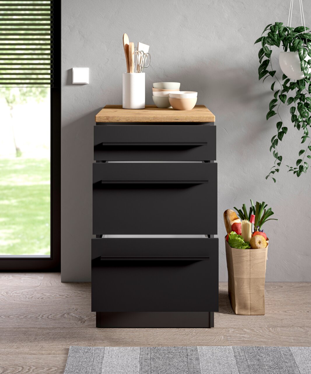 Moderner Unterschrank 50A in dunklem Design mit Holzplatte, frontal fotografiert, dekoriert mit Küchenutensilien und Schalen, neben einer Pflanze und einer Einkaufstüte.