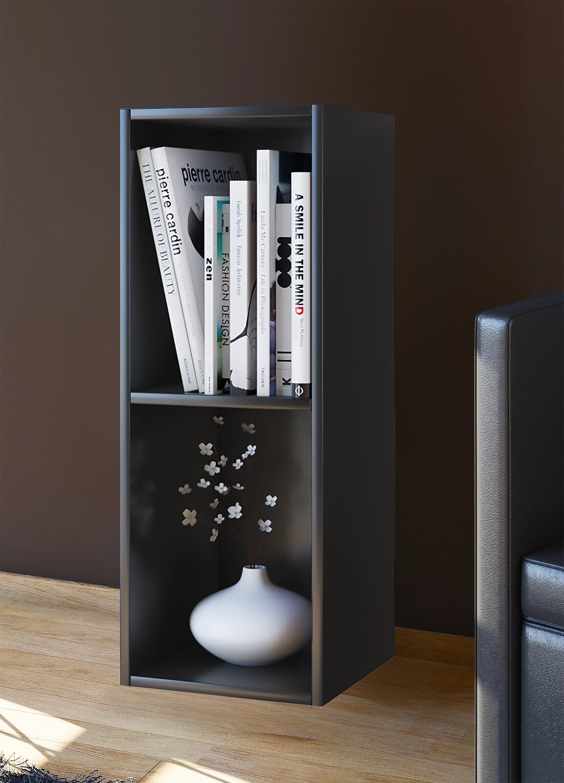 Schmales, modernes Regal in Dunkelgrau/Schwarz mit zwei offenen Fächern, oben mit Büchern und unten mit weißer Vase und Zweigen, Innenraumansicht aus leicht schräger Frontperspektive.