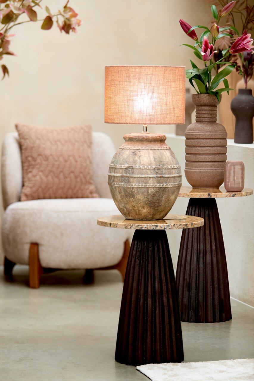 Rustikaler Lampenschirm auf antikem Keramikfuß, seitliche Perspektive, umgeben von moderner Einrichtung und Blumen.