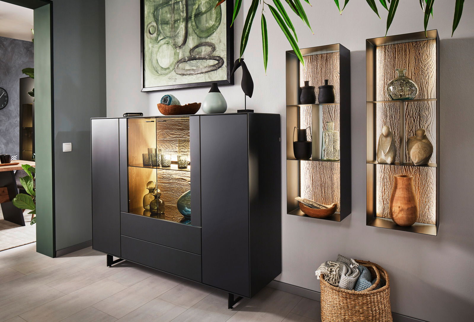 Valnatura Highboard LIVINO Modernes Highboard in dunklem Design mit Glasvitrine, dekoriert mit Keramik und Glasobjekten, aus seitlicher Perspektive fotografiert.