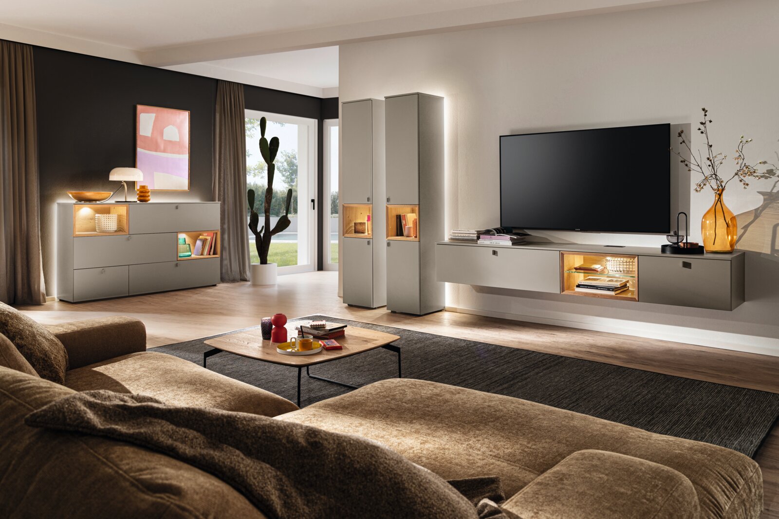 Moderne Wohnzimmer-Wandkombination in neutralen Tönen mit TV-Schrank, Vitrinen und Sideboard, aus der Perspektive eines gemütlichen Wohnzimmers mit Sofa und Couchtisch.