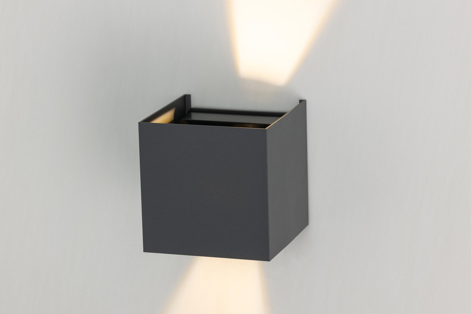 Moderne LED-Wandleuchte in kubischer Form, die sowohl nach oben als auch nach unten Licht abstrahlt. Perspektive von schräg vorne.