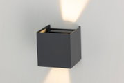 Moderne LED-Wandleuchte in kubischer Form, die sowohl nach oben als auch nach unten Licht abstrahlt. Perspektive von schräg vorne.