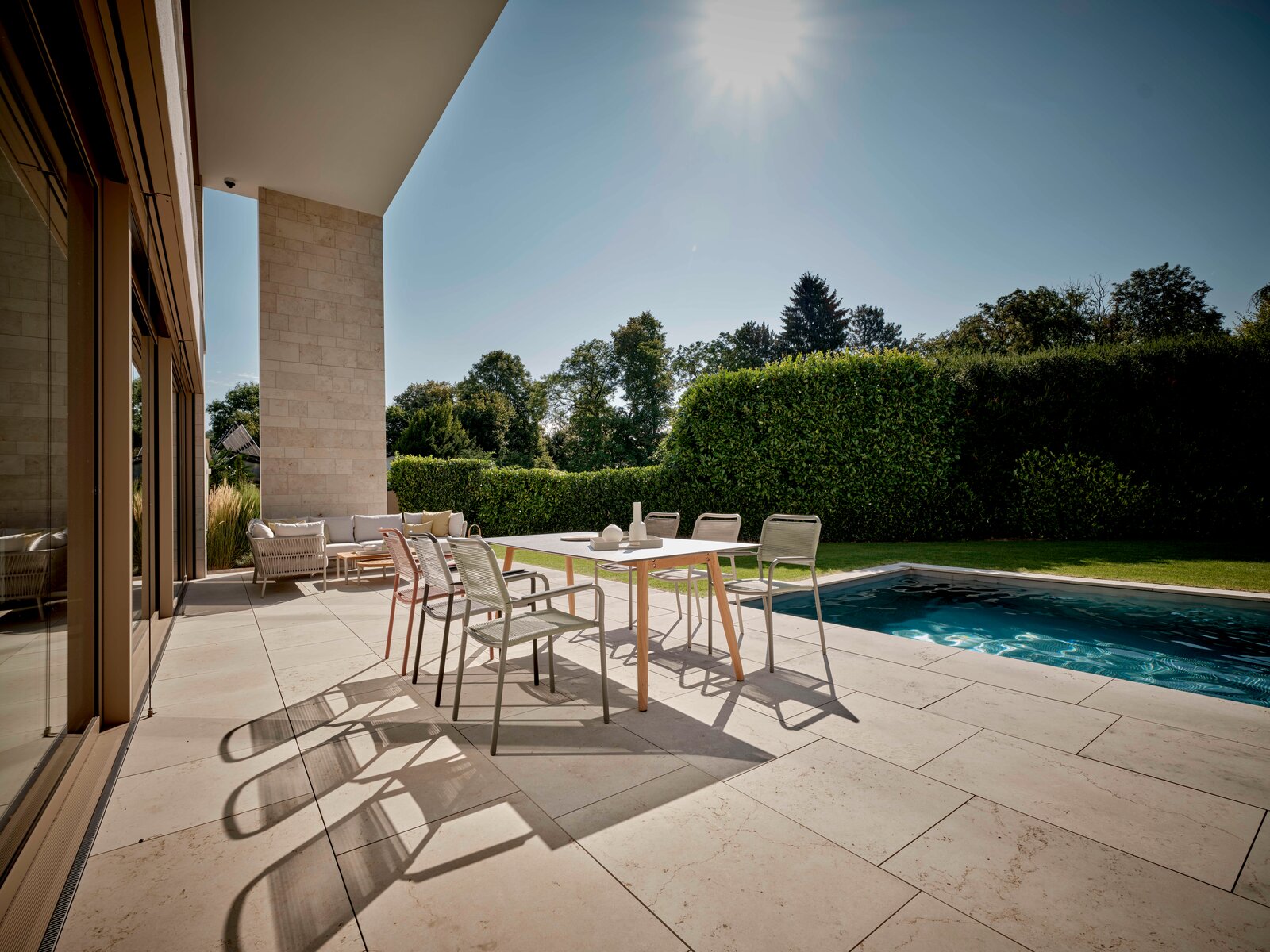 Moderner Stapelsessel auf einer sonnigen Terrasse mit Blick auf einen Pool und Garten.