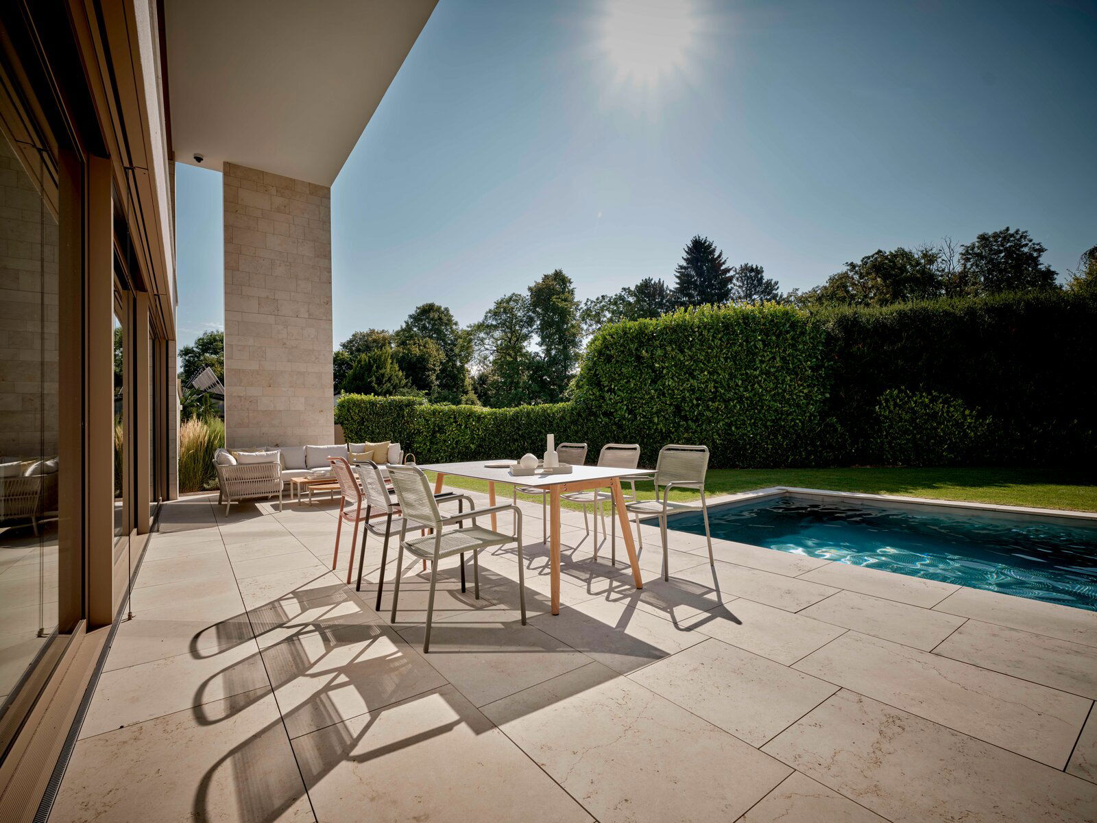 Moderner Stapelsessel auf einer sonnigen Terrasse mit Blick auf einen Pool und Garten.