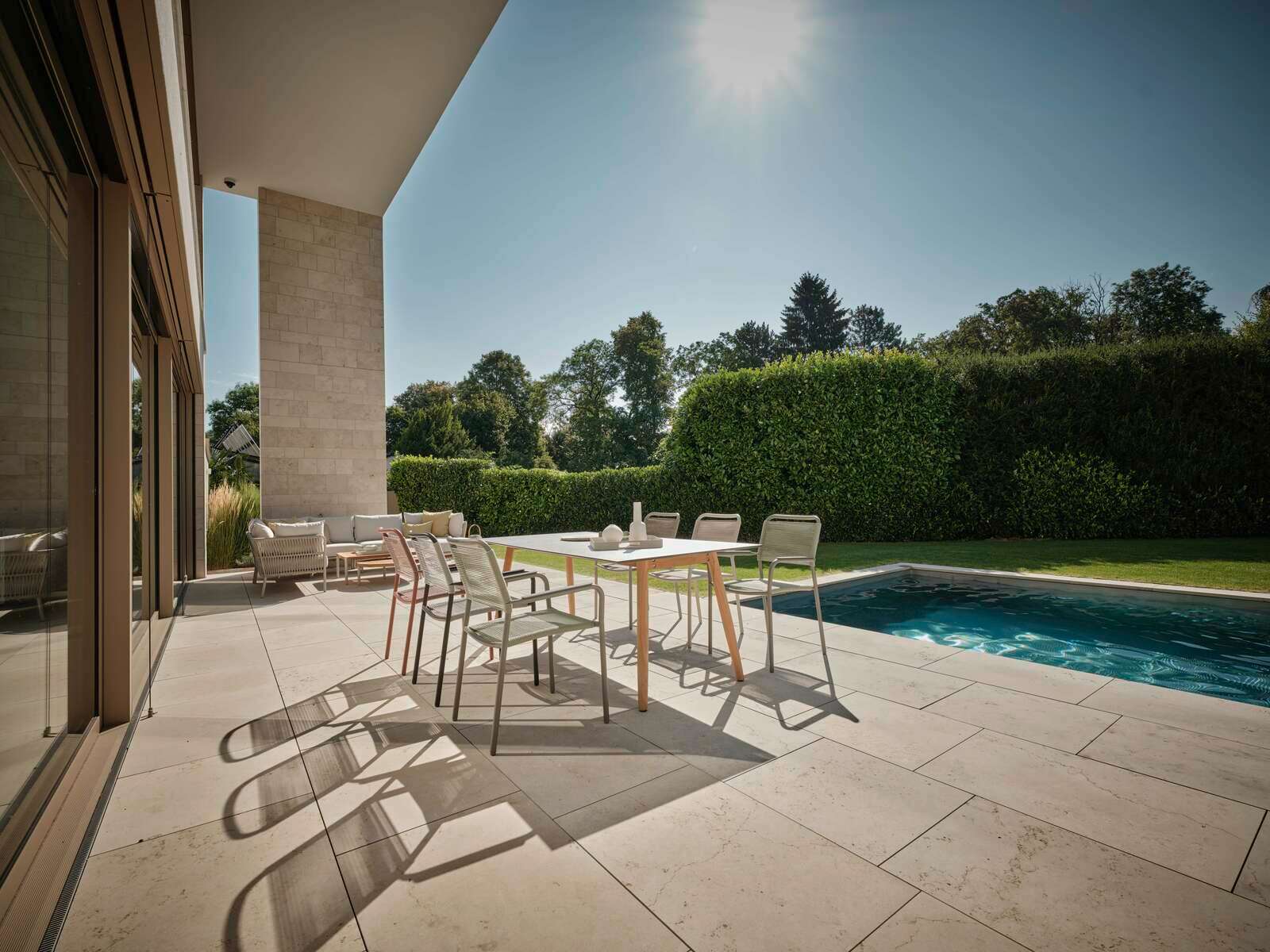Moderner Stapelsessel auf einer sonnigen Terrasse mit Blick auf einen Pool und Garten.