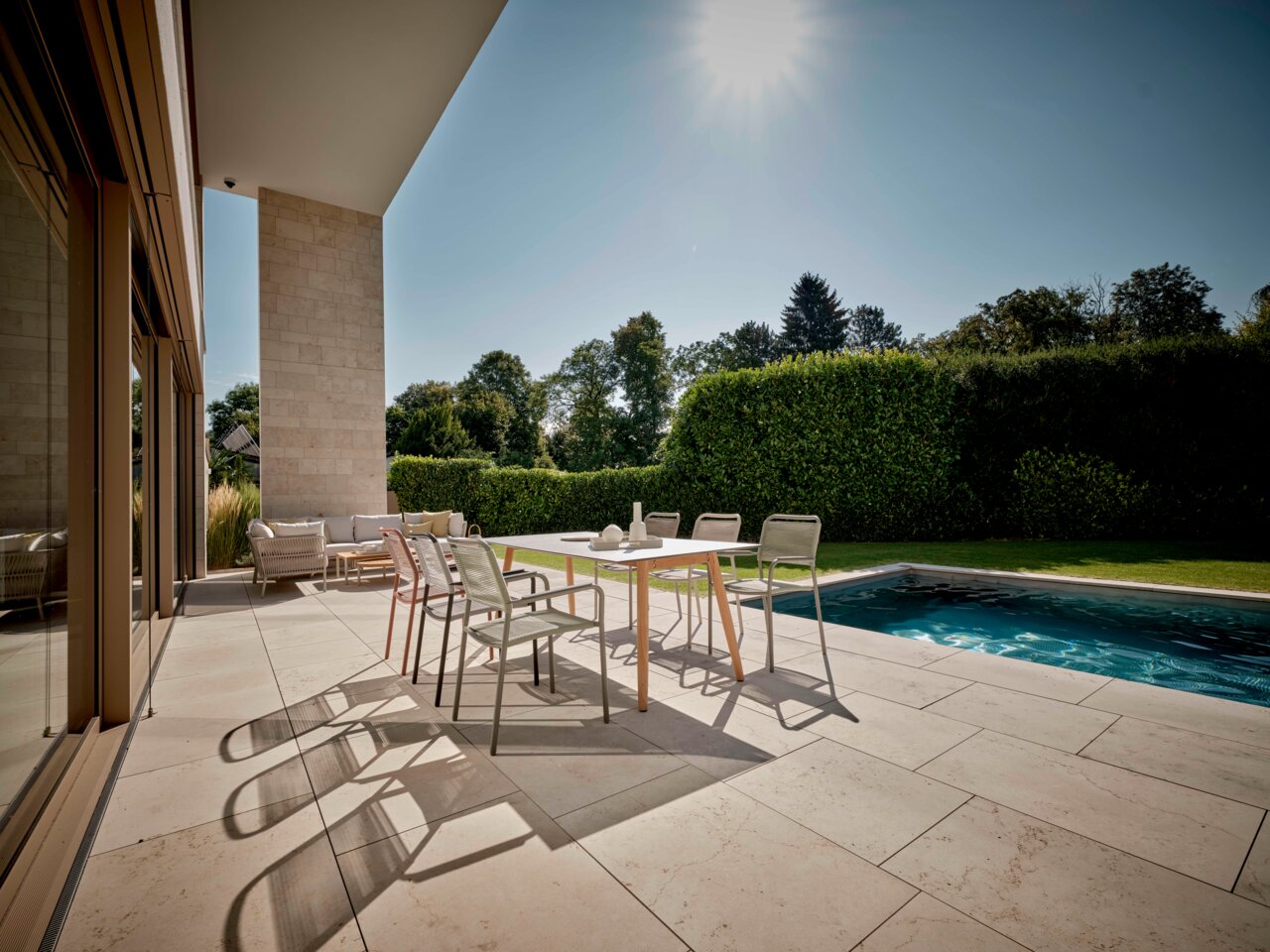 Stern Stapelsessel JORIS Moderner Stapelsessel auf einer sonnigen Terrasse mit Blick auf einen Pool und Garten.