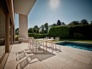 Moderner Stapelsessel auf einer sonnigen Terrasse mit Blick auf einen Pool und Garten.