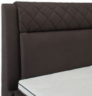 Nahaufnahme eines Boxspringbettes mit gestepptem Kopfteil in dunklem Stoff und weißer Matratze, seitliche Perspektive