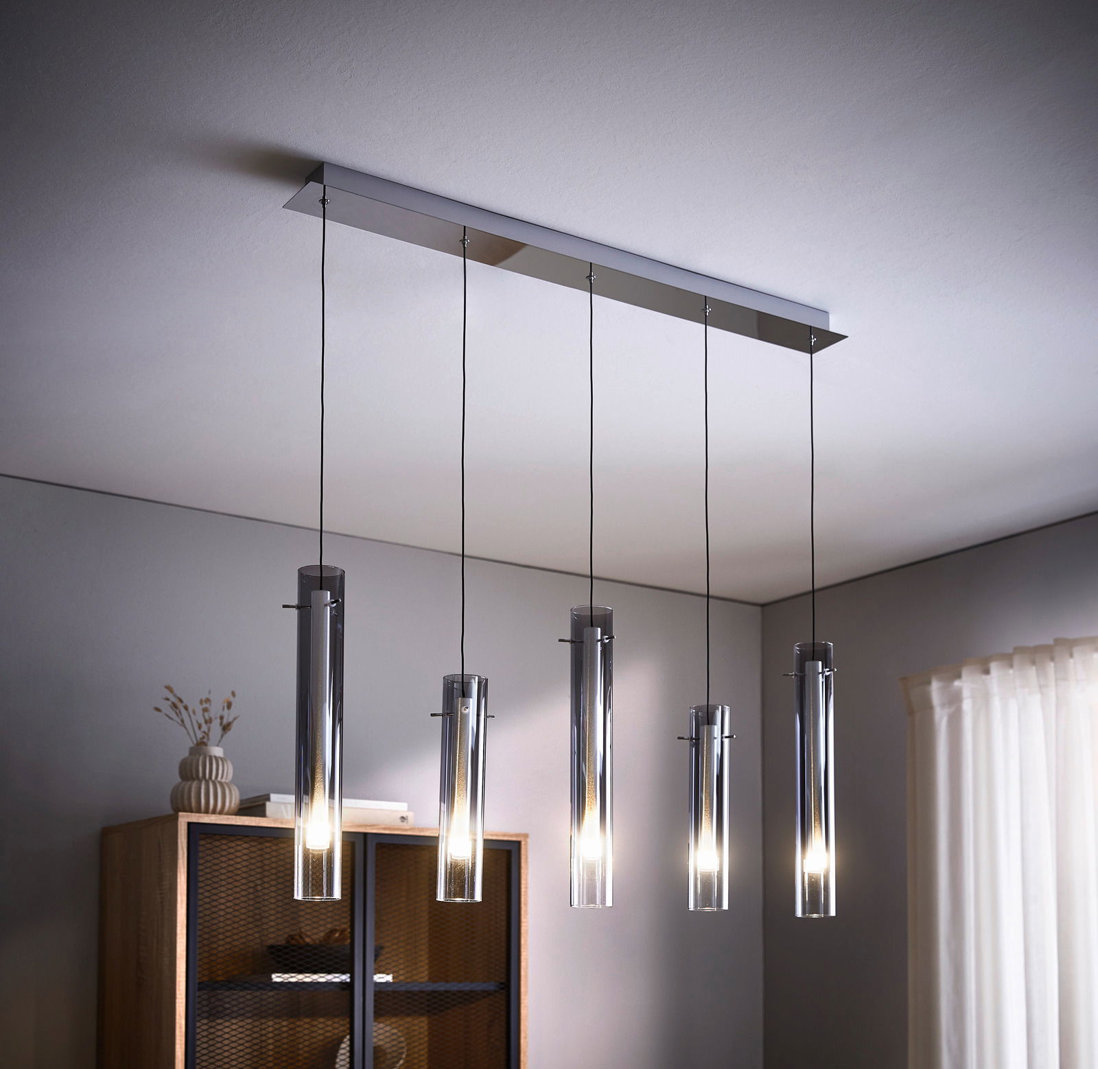 Moderne LED-Hängeleuchte mit fünf zylindrischen Lampen, aufgehängt an dünnen Kabeln, in einem stilvollen Wohnraum von unten betrachtet.