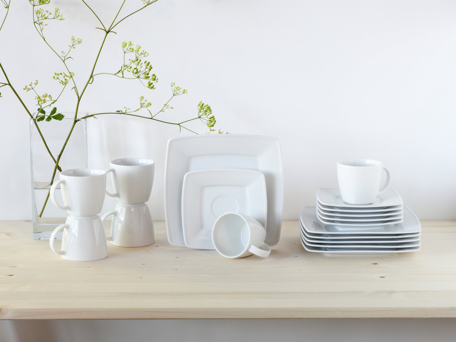 Creatable Kaffeeservice 18-tlg VICTORIA Weißes, quadratisches Porzellan-Geschirrset mit Tellern und Tassen auf hellem Holztisch vor weißem Hintergrund, perspektive: frontale Ansicht auf Augenhöhe.