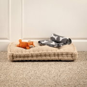 Hundespielzeug-Set mit orangefarbenem Plüschfuchs und grauer Decke mit Knochenmuster auf beigem Hundebett, seitliche Perspektive