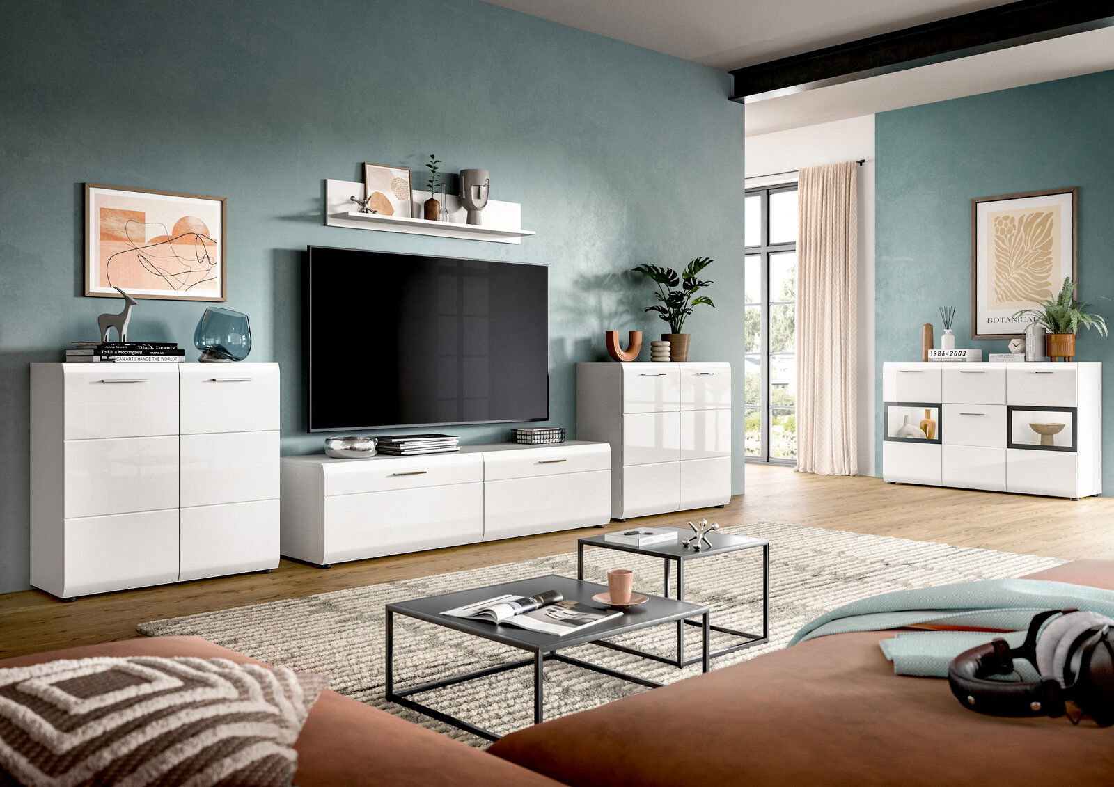 Modernes Wohnzimmer mit weißer, hochglänzender TV-Wohnwand (Lowboard, Highboards und Sideboard) vor petrolfarbener Wand, großer Fernseher mittig; Perspektive: frontale, leicht seitliche Weitwinkelansicht auf die Möbelgruppe.