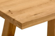 Nahaufnahme einer massiven Holz-Tischplatte mit sichtbarer Maserung und Astlöchern, schräg von oben auf die Ecke des Tisches fotografiert