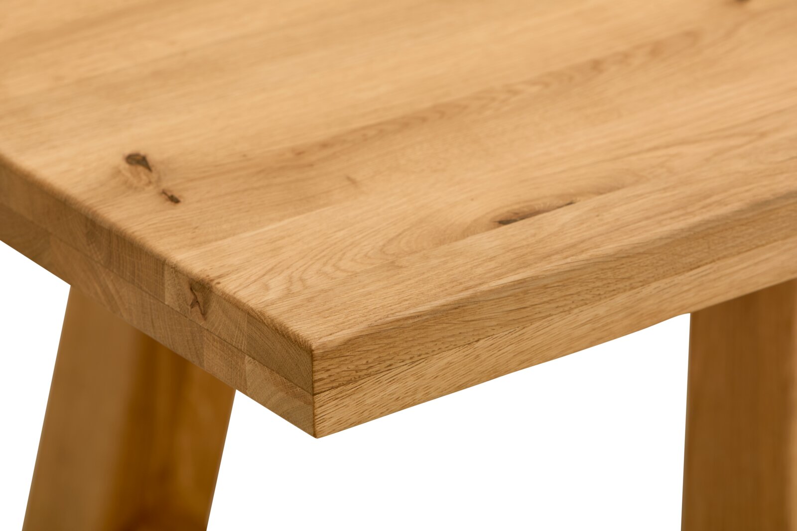 Nahaufnahme einer massiven Holz-Tischplatte mit sichtbarer Maserung und Astlöchern, schräg von oben auf die Ecke des Tisches fotografiert