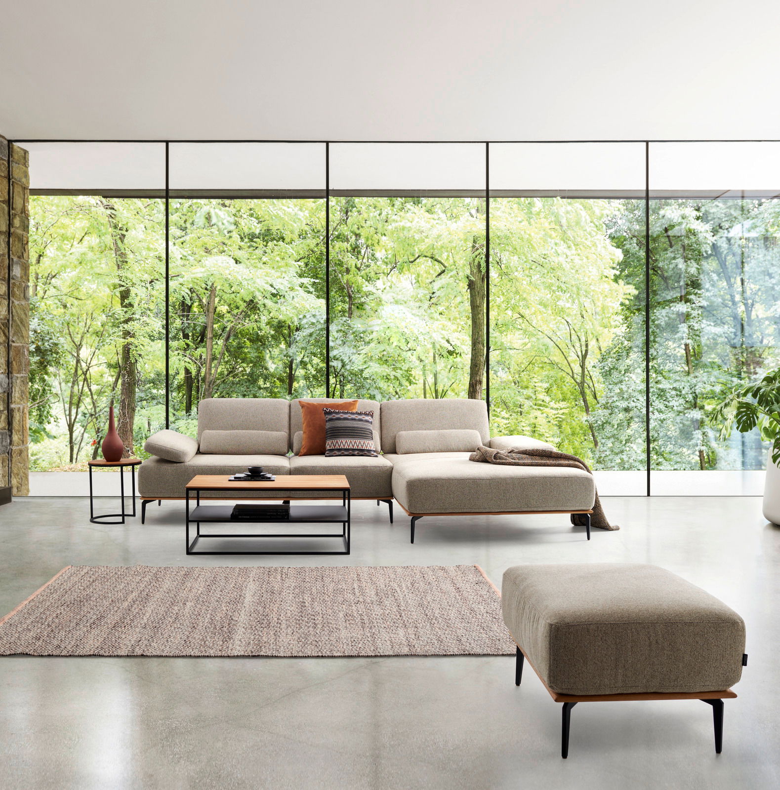 Großer Valnatura Hocker SPRINT in einem modernen Wohnzimmer mit großen Fenstern und Blick auf einen grünen Wald, Perspektive von vorne.