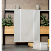 Beige Geschirrtuch mit dezentem Muster, aufgehängt vor einer Holzwand mit Pflanzen im Hintergrund, Vorderansicht