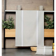 Beige theedoek met subtiel patroon, opgehangen voor een houten wand met planten op de achtergrond, vooraanzicht