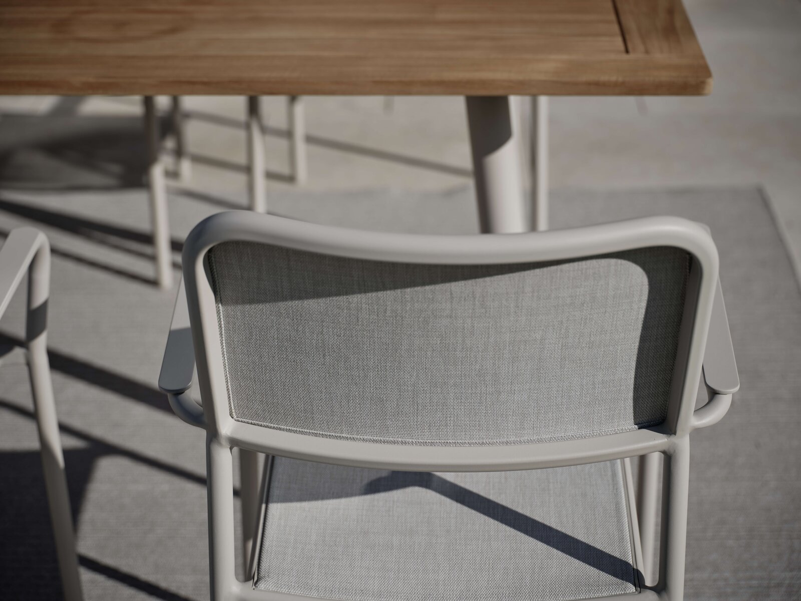 Rückansicht eines grauen Stapelsessels mit Armlehnen, im Freien neben einem Holztisch.