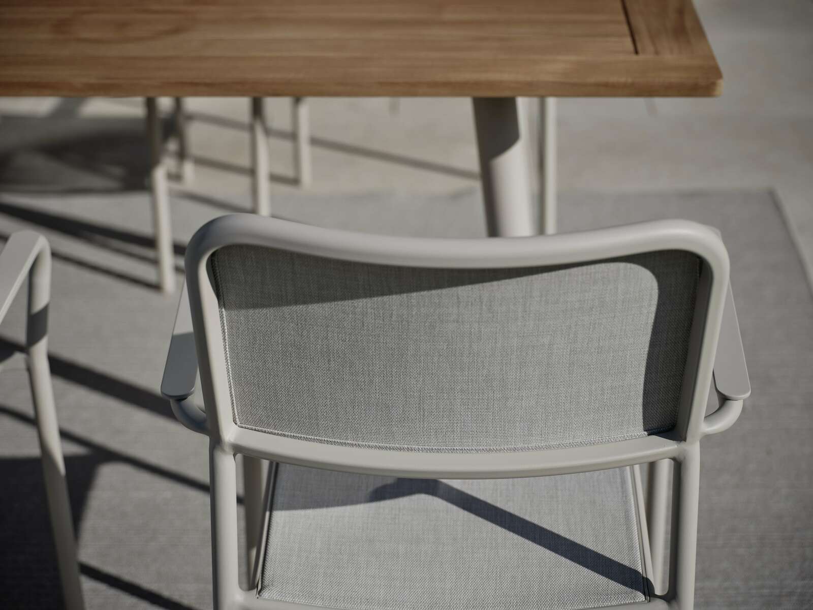 Rückansicht eines grauen Stapelsessels mit Armlehnen, im Freien neben einem Holztisch.