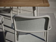 Rückansicht eines grauen Stapelsessels mit Armlehnen, im Freien neben einem Holztisch.