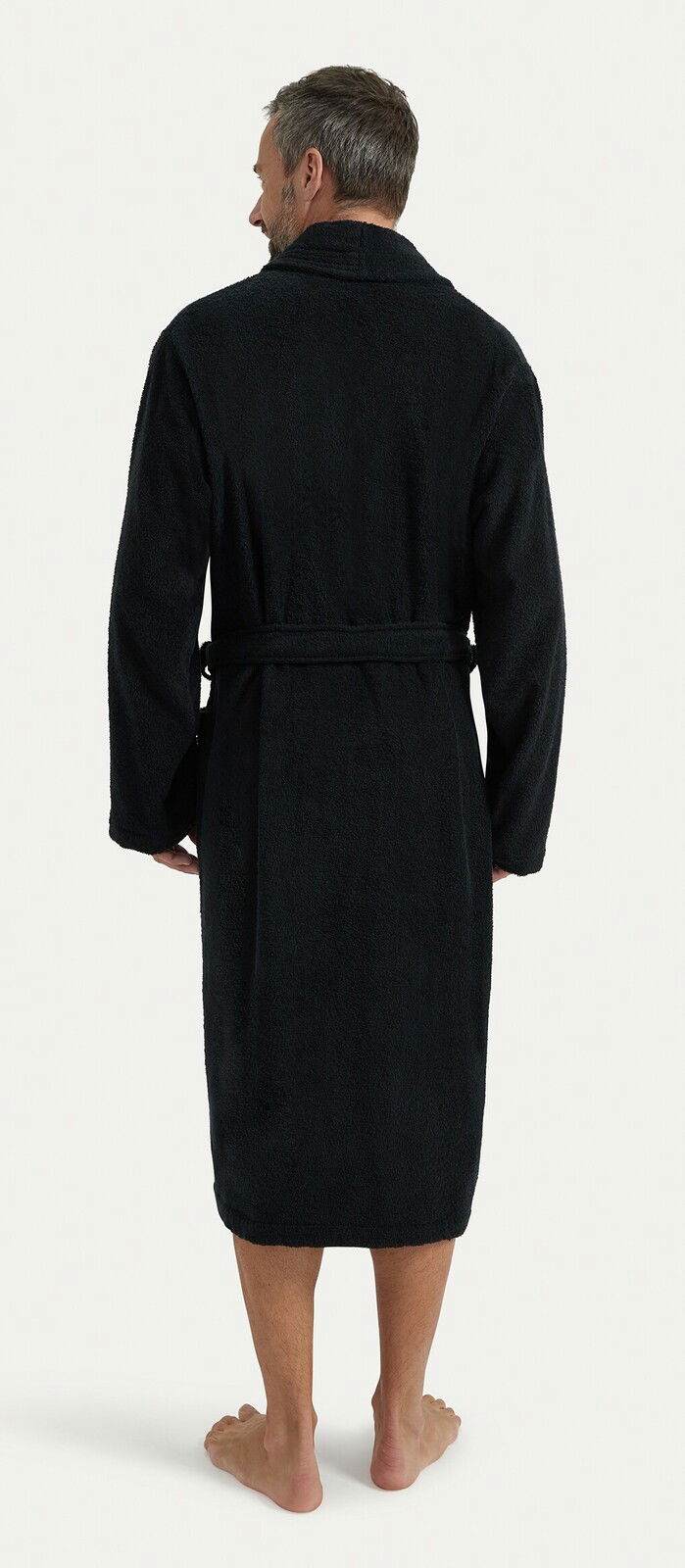 Rückansicht eines Mannes in einem schwarzen Bademantel mit Schalkragen, der bis zu den Waden reicht.