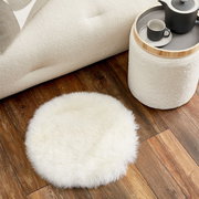 Rundes Schaffell Sitzkissen auf Holzboden, von oben betrachtet, neben einem Sofa und einem Beistelltisch.