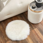 Rundes Schaffell Sitzkissen auf Holzboden, von oben betrachtet, neben einem Sofa und einem Beistelltisch.