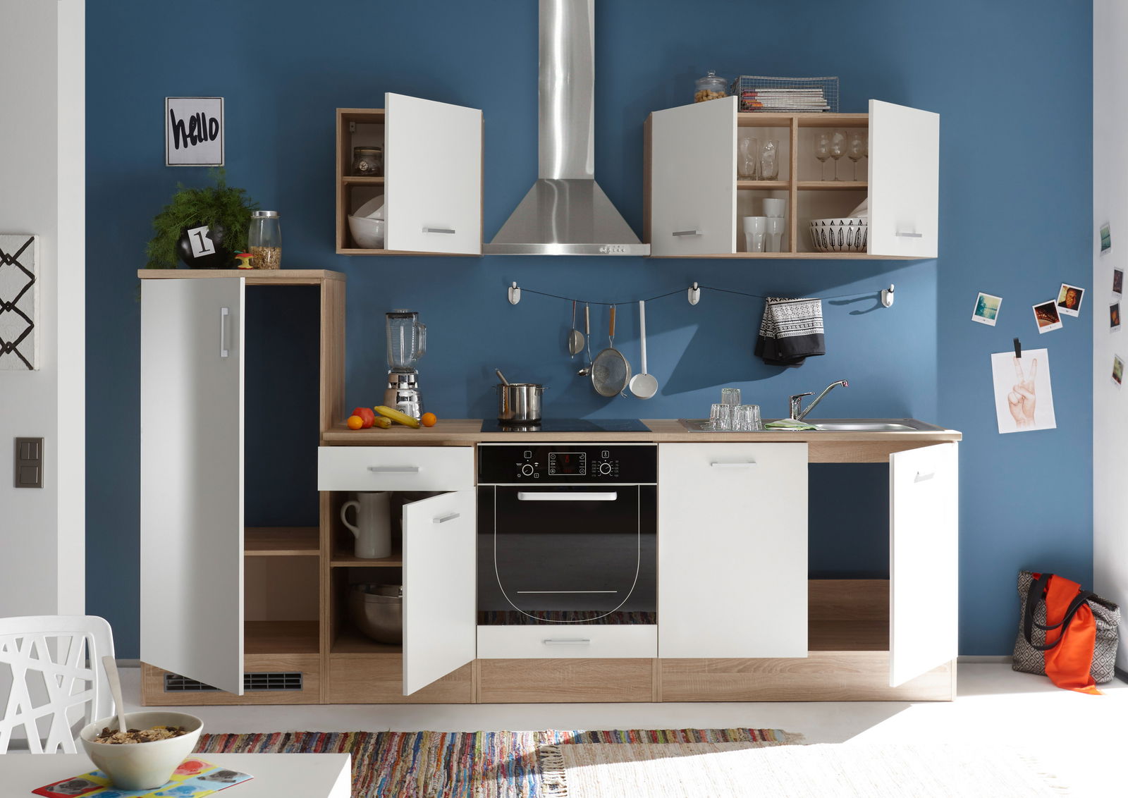 Moderne Küchenzeile mit weißen und holzfarbenen Schränken, Edelstahl-Dunstabzugshaube und blauer Wand im Hintergrund, frontale Perspektive.