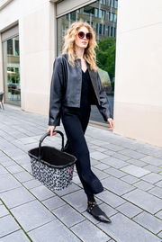 Frau in schwarzer Kleidung trägt einen Einkaufskorb mit Leopardenmuster auf der Straße, seitliche Perspektive.