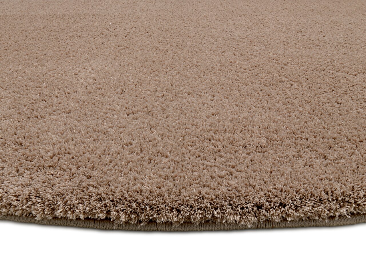 Nahaufnahme eines runden, beigen Teppichs mit weicher, flauschiger Textur, seitliche Perspektive.